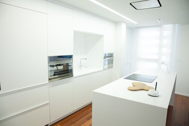 Modelo de cocina lineal contemporánea de tamaño medio cerrada con armarios con paneles lisos, puertas de armario blancas, salpicadero blanco, electrodomésticos de acero inoxidable, suelo de madera en tonos medios y una isla