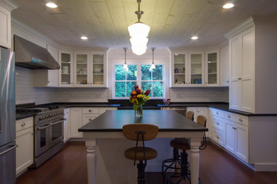Example of a large country u-shaped dark wood floor and wood ceiling eat-in kitchen design in Philadelphia with a farmhouse sink, shaker cabinets, white cabinets, soapstone countertops, white backsplash, ceramic backsplash, stainless steel appliances and an island