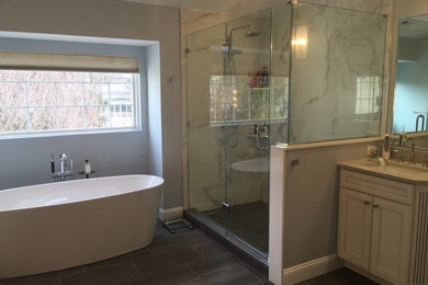 Modelo de cuarto de baño principal actual grande con puertas de armario blancas, bañera exenta, encimera de cuarzo compacto, lavabo encastrado, paredes grises y ducha esquinera