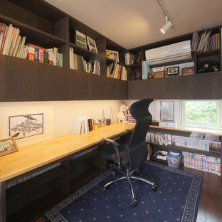 This is an example of a large modern study in Other with brown walls, plywood flooring, no fireplace, a built-in desk and brown floors.