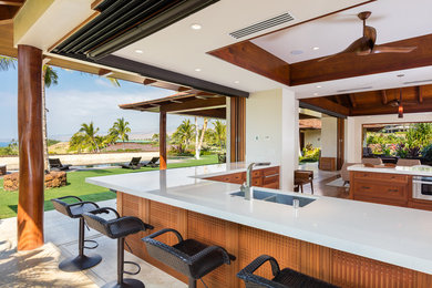Inspiration for a large tropical l-shaped open plan kitchen in Hawaii with a double-bowl sink, recessed-panel cabinets, medium wood cabinets, quartz benchtops, stainless steel appliances, limestone floors and a peninsula.