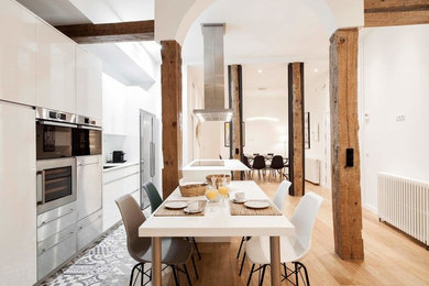Large industrial single-wall open plan kitchen in Madrid with flat-panel cabinets, white cabinets, stainless steel appliances, ceramic floors, with island, multi-coloured floor and white benchtop.