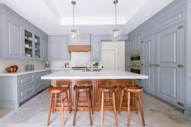 Example of a large classic u-shaped limestone floor and beige floor enclosed kitchen design in New York with a farmhouse sink, raised-panel cabinets, blue cabinets, quartz countertops, white backsplash, ceramic backsplash, paneled appliances, an island and white countertops