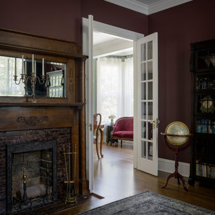 Modelo de despacho tradicional con suelo de madera en tonos medios, estufa de leña, marco de chimenea de ladrillo, escritorio independiente y suelo marrón