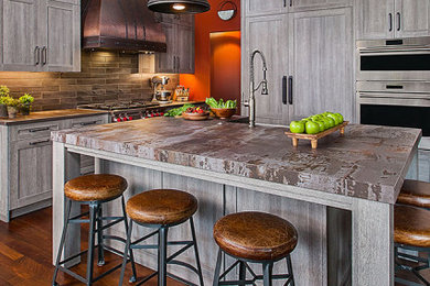 Inspiration for a large rustic l-shaped medium tone wood floor and brown floor eat-in kitchen remodel in Detroit with a farmhouse sink, shaker cabinets, distressed cabinets, brown backsplash, porcelain backsplash, stainless steel appliances, an island and multicolored countertops