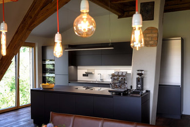 Offene, Große, Einzeilige Moderne Küche mit flächenbündigen Schrankfronten, schwarzen Schränken, Küchenrückwand in Weiß, dunklem Holzboden, Kücheninsel, braunem Boden, schwarzer Arbeitsplatte, Einbauwaschbecken und Küchengeräten aus Edelstahl in Sonstige