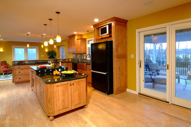 Example of a classic l-shaped light wood floor kitchen design in Philadelphia with a farmhouse sink, raised-panel cabinets, medium tone wood cabinets, granite countertops, multicolored backsplash, stone tile backsplash, black appliances and an island