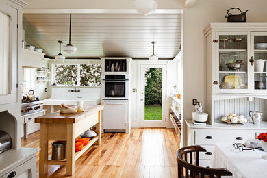 Inspiration for a mid-sized country u-shaped medium tone wood floor and brown floor eat-in kitchen remodel in Portland with wood countertops, white backsplash, white appliances, an island and beige countertops