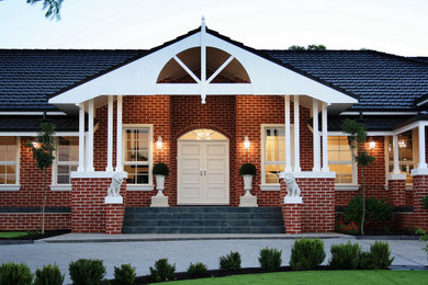 This is an example of a traditional one-storey red house exterior in Other with a tile roof and a black roof.