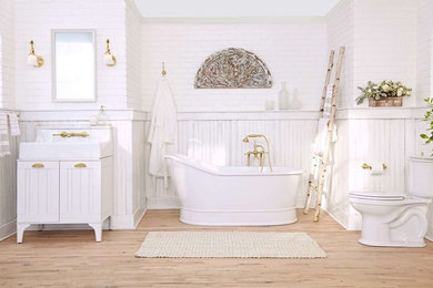 Inspiration for a large cottage master medium tone wood floor and beige floor freestanding bathtub remodel in New York with white cabinets, a two-piece toilet, white walls, a drop-in sink and marble countertops