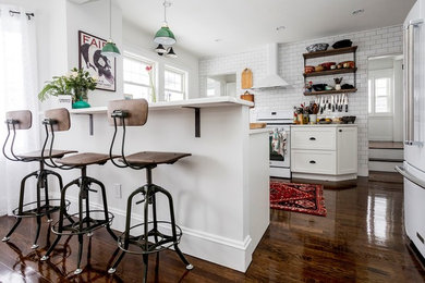 Inspiration for a mid-sized cottage u-shaped medium tone wood floor and brown floor eat-in kitchen remodel in Boston with a farmhouse sink, shaker cabinets, white cabinets, quartz countertops, white backsplash, subway tile backsplash, white appliances, a peninsula and white countertops