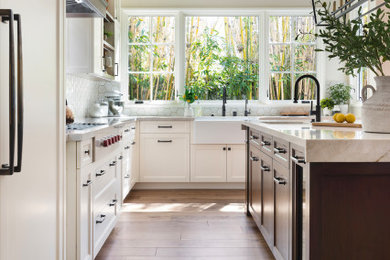 Eat-in kitchen - large transitional u-shaped medium tone wood floor and brown floor eat-in kitchen idea in Los Angeles with a farmhouse sink, shaker cabinets, brown cabinets, quartzite countertops, white backsplash, stone tile backsplash, stainless steel appliances, an island and beige countertops