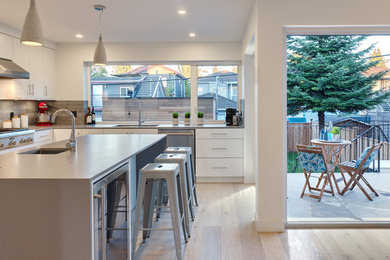 Eat-in kitchen - mid-sized contemporary l-shaped light wood floor eat-in kitchen idea in Vancouver with a double-bowl sink, flat-panel cabinets, white cabinets, quartz countertops, white backsplash, stone tile backsplash, stainless steel appliances and an island