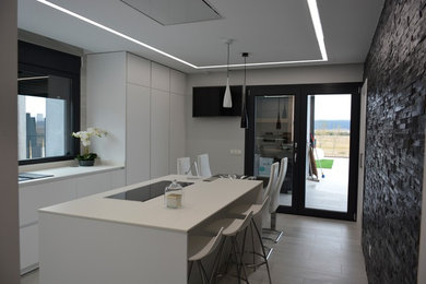 Modelo de cocina contemporánea cerrada con fregadero bajoencimera, armarios con paneles lisos, puertas de armario blancas, electrodomésticos blancos, suelo de baldosas de cerámica y una isla