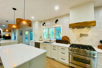 Klassisk inredning av ett stort vit vitt kök, med en undermonterad diskho, skåp i shakerstil, vita skåp, bänkskiva i kvarts, flerfärgad stänkskydd, stänkskydd i trä, rostfria vitvaror, ljust trägolv, flera köksöar och flerfärgat golv