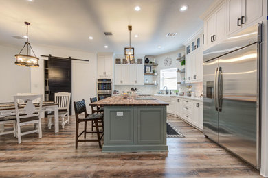 Large cottage u-shaped vinyl floor, brown floor and vaulted ceiling eat-in kitchen photo in Houston with shaker cabinets, white cabinets, an island, a farmhouse sink, quartzite countertops, white backsplash, mosaic tile backsplash, stainless steel appliances and white countertops