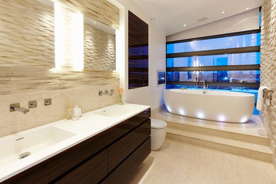 Large contemporary bathroom in London with an integrated sink, flat-panel cabinets, dark wood cabinets, solid surface benchtops, a freestanding tub, a corner shower, a one-piece toilet, beige tile, stone slab, white walls and limestone floors.