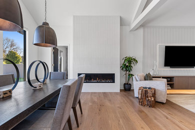 Inspiration for a large contemporary medium tone wood floor, brown floor, vaulted ceiling and wood wall kitchen/dining room combo remodel in Other with white walls, a standard fireplace and a tile fireplace