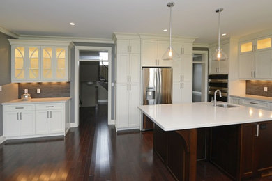 Example of a minimalist dark wood floor and brown floor eat-in kitchen design with an integrated sink, glass-front cabinets, white cabinets, quartzite countertops, gray backsplash, stainless steel appliances, white countertops and stone tile backsplash