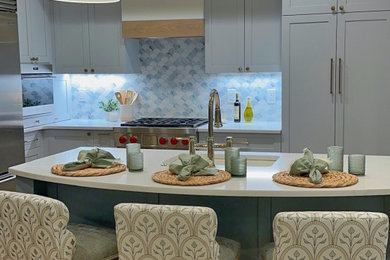 This is an example of a small contemporary l-shaped kitchen/diner in New York with a submerged sink, shaker cabinets, blue cabinets, engineered stone countertops, blue splashback, glass tiled splashback, stainless steel appliances, medium hardwood flooring, an island, brown floors and white worktops.