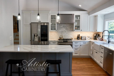 Modern l-shaped eat-in kitchen in New York with a farmhouse sink, shaker cabinets, white cabinets, quartzite benchtops, grey splashback, marble splashback, stainless steel appliances, medium hardwood floors, with island and white benchtop.