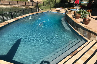 This is an example of a mid-sized backyard custom-shaped natural pool in Dallas with a hot tub and natural stone pavers.
