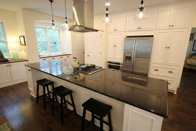 Example of a classic l-shaped medium tone wood floor open concept kitchen design in Other with a farmhouse sink, raised-panel cabinets, white cabinets, granite countertops, white backsplash, subway tile backsplash, stainless steel appliances, an island and black countertops