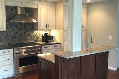 Eat-in kitchen - mid-sized traditional l-shaped dark wood floor eat-in kitchen idea in New York with an undermount sink, raised-panel cabinets, white cabinets, granite countertops, multicolored backsplash, stone tile backsplash, stainless steel appliances and an island