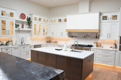 This is an example of an expansive contemporary u-shaped open plan kitchen in DC Metro with an undermount sink, recessed-panel cabinets, white cabinets, white splashback, stainless steel appliances, medium hardwood floors, multiple islands, brown floor and white benchtop.