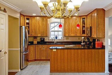 Inspiration for a timeless u-shaped vinyl floor and gray floor eat-in kitchen remodel in Baltimore with a double-bowl sink, shaker cabinets, medium tone wood cabinets, granite countertops, stainless steel appliances, a peninsula and black countertops