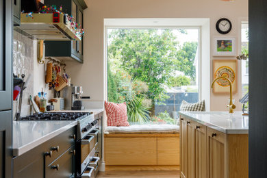 Design ideas for a medium sized contemporary single-wall kitchen/diner in Dublin with a belfast sink, flat-panel cabinets, medium wood cabinets, granite worktops, green splashback, glass sheet splashback, integrated appliances, light hardwood flooring, an island, multi-coloured floors and exposed beams.