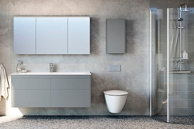 Inredning av ett vit vitt badrum med dusch, med släta luckor, grå skåp, en hörndusch, en vägghängd toalettstol, grå kakel, grå väggar, klinkergolv i småsten, bänkskiva i akrylsten, grått golv och dusch med gångjärnsdörr