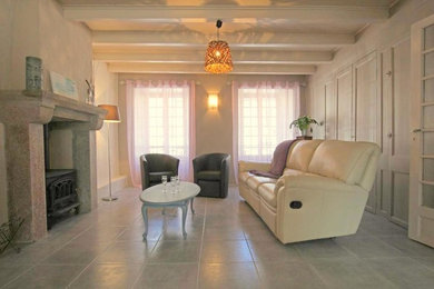 Aménagement d'un salon bord de mer de taille moyenne et ouvert avec un mur beige, un sol en carrelage de céramique, un poêle à bois, un manteau de cheminée en pierre, un téléviseur indépendant et un sol gris.