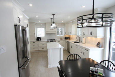 This is an example of a large contemporary u-shaped eat-in kitchen in Toronto with an undermount sink, recessed-panel cabinets, white cabinets, quartz benchtops, white splashback, engineered quartz splashback, stainless steel appliances, porcelain floors, with island, grey floor and white benchtop.