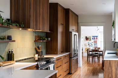 Kitchen - contemporary u-shaped medium tone wood floor and brown floor kitchen idea in Louisville with an undermount sink, flat-panel cabinets, medium tone wood cabinets, green backsplash, stainless steel appliances, a peninsula and white countertops