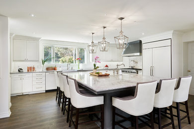 Photo of a transitional l-shaped kitchen in Toronto with a farmhouse sink, shaker cabinets, white cabinets, white splashback, panelled appliances, dark hardwood floors, with island and brown floor.