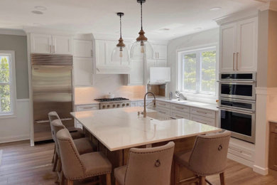 Inspiration for a mid-sized french country l-shaped medium tone wood floor and multicolored floor eat-in kitchen remodel in Philadelphia with a farmhouse sink, shaker cabinets, white cabinets, quartz countertops, white backsplash, quartz backsplash, stainless steel appliances, an island and white countertops