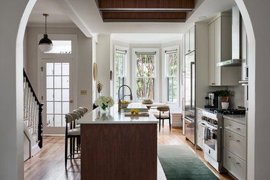 Example of a mid-sized trendy single-wall medium tone wood floor eat-in kitchen design in DC Metro with an island, white cabinets, stainless steel appliances and white countertops
