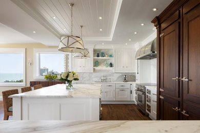 Inspiration for a large beach style l-shaped open plan kitchen in Miami with an undermount sink, recessed-panel cabinets, white cabinets, marble benchtops, grey splashback, marble splashback, panelled appliances, medium hardwood floors, with island, brown floor and grey benchtop.