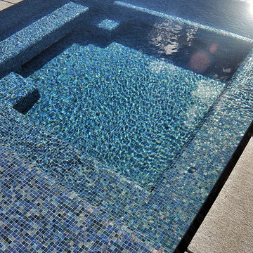 glass tile swimming pool + spa with perimeter overflow + granite decking