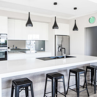 Large modern galley kitchen pantry in Sydney with a drop-in sink, flat-panel cabinets, white cabinets, quartz benchtops, black splashback, glass sheet splashback, stainless steel appliances, plywood floors, with island and grey floor.