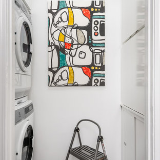 Photo of a small contemporary galley laundry cupboard in Atlanta with flat-panel cabinets, white cabinets, bamboo flooring, grey floors, white walls and a stacked washer and dryer.