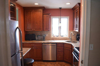 Example of a small classic u-shaped porcelain tile and brown floor enclosed kitchen design in New York with an undermount sink, raised-panel cabinets, medium tone wood cabinets, granite countertops, beige backsplash, stone tile backsplash, stainless steel appliances and a peninsula