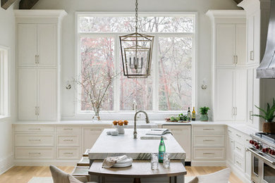 Inspiration for a country l-shaped eat-in kitchen in Atlanta with a farmhouse sink, recessed-panel cabinets, white cabinets, white splashback, window splashback, stainless steel appliances, medium hardwood floors, with island, brown floor, white benchtop and quartz benchtops.