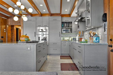 Mid-sized eclectic l-shaped eat-in kitchen in New York with flat-panel cabinets, grey cabinets, stainless steel appliances, with island and exposed beam.