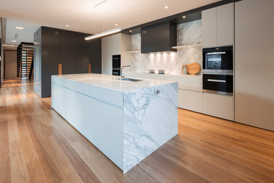 Photo of a large contemporary galley kitchen pantry in Canberra - Queanbeyan with an undermount sink, marble benchtops, white splashback, stainless steel appliances, light hardwood floors and with island.