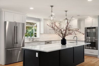 Example of a transitional light wood floor and brown floor open concept kitchen design in Seattle with an undermount sink, flat-panel cabinets, white cabinets, quartzite countertops, white backsplash, ceramic backsplash, stainless steel appliances, an island and white countertops