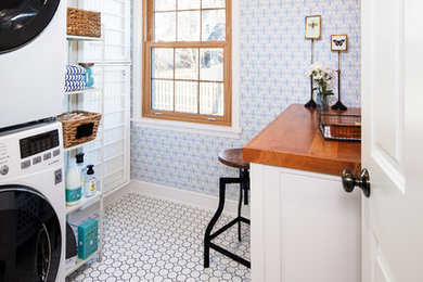 Inspiration for a traditional single-wall dedicated laundry room in Omaha with white cabinets, wood benchtops, blue walls, a stacked washer and dryer, white floor and brown benchtop.