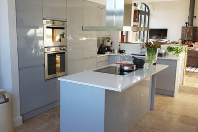 Inspiration for a medium sized contemporary l-shaped open plan kitchen in West Midlands with an integrated sink, flat-panel cabinets, grey cabinets, quartz worktops, white splashback, stone slab splashback, stainless steel appliances, limestone flooring, an island and white worktops.