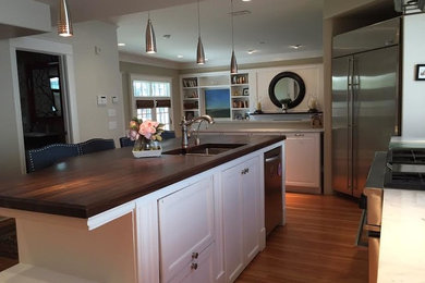 This is an example of a large contemporary l-shaped eat-in kitchen in Denver with an undermount sink, raised-panel cabinets, white cabinets, wood benchtops, white splashback, stainless steel appliances, light hardwood floors, with island, multi-coloured floor and brown benchtop.